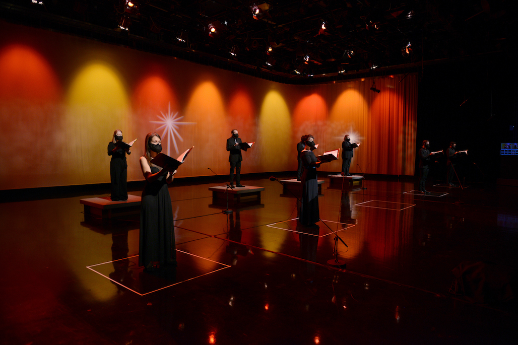 Six performers, spaced six feet apart, perform “Messiah” in GBH studio lit with soft golden lighting.